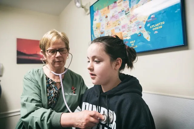 a pediatrician listening to a young teens heart